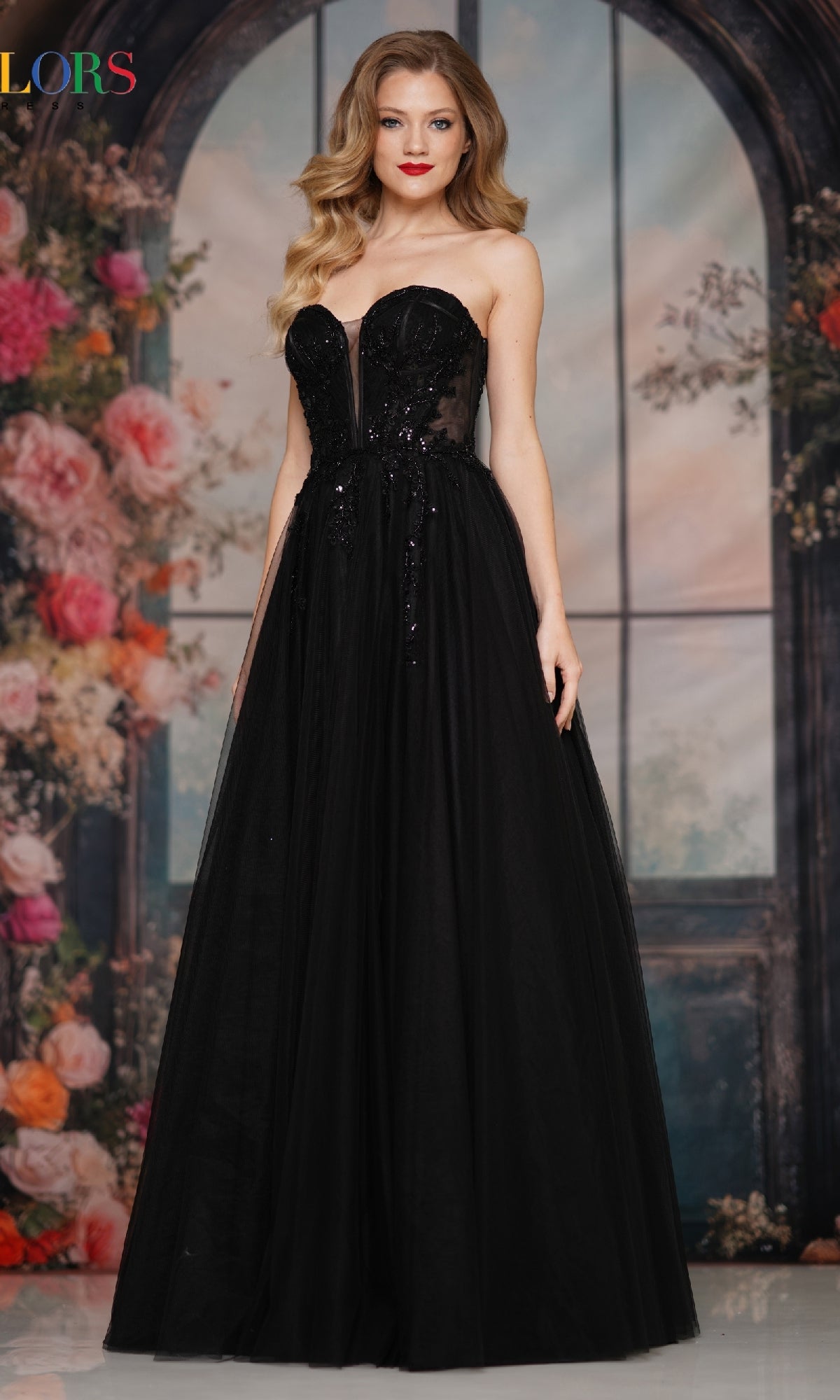 A woman in the Strapless Long Corset Prom Dress: Colors Dress 3923 stands before a floral and arched window backdrop.